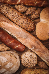 Many mixed baked breads and rolls on rustic wooden table