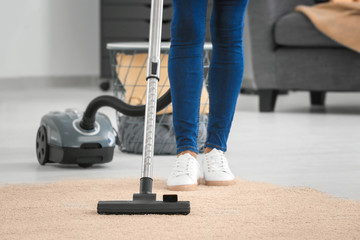 Woman hoovering carpet with vacuum cleaner at home