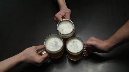 Three men drinking lager near the bar counter. Close up of male hands clinking their glasses top...