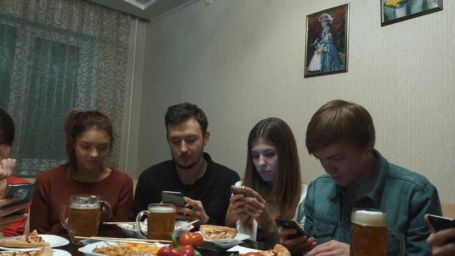 Gadget device addiction, friends dinner with smarphones, online in social networks while eating food together, wooden table. Group of friends at a restaurant with all people on the table occupied with