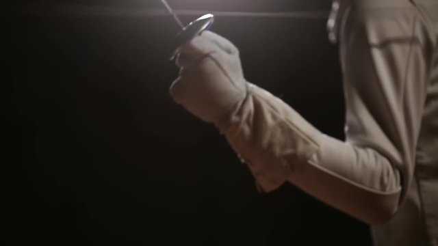 Closeup of a rapier for fencing in the hand performs offensive movements. Male swordsman attacks. Side view. Beautiful backlighting.