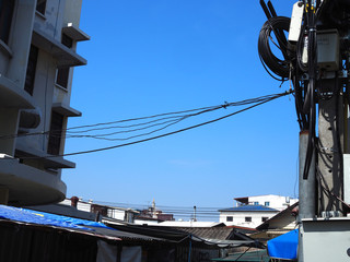 Clear blue gradient winter sky with old style building and messy electrical pole on both sides, and small house roof, dirty aluminum corrugated wall with plastic canvas shade, power line cord crossing