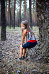 Little beautiful girl sitting on a stump in a pine forest