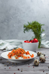 delicious rice with stewed carrots, peas and onions on a white plate, quail eggs, bowl with cherry tomatoes, towel, pepper and dill on a light wooden table