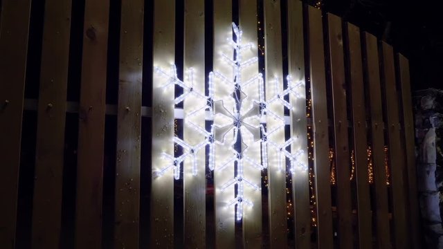 A snowflake made from Christmas lights hanging on the wooden fence. HD