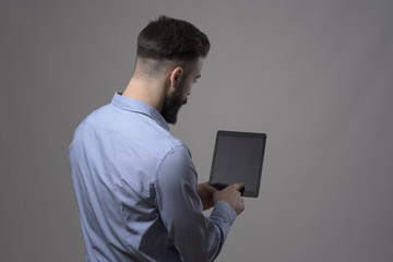 Rear view of young business man touching blank tablet display with index finger against gray studio...
