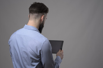 Over the shoulder view of young business man holding and reading blank tablet computer over gray...