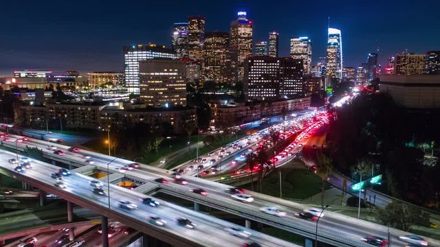 Cinematic urban aerial drone time lapse in motion of downtown Los Angeles freeways with heavy traffic, city skyline and sky scrapers at night with deep blue sky.