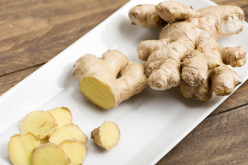 Ginger cut on a white plate, on wooden table. Food