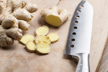 Ginger next to kitchen knife on wood. Food