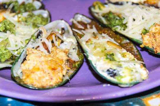 Assorted multicolored baked mussels on a violet plate on a tablecloth space