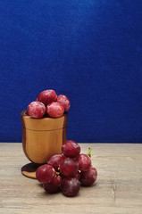 Red grapes displayed in a wooden bowl isolated against a blue background