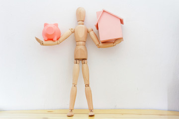 Business and financial concept. Dummy / ball jointed doll holding toy wooden house and piggy bank