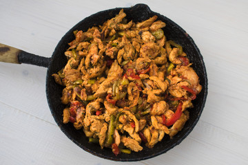 Chicken stew with red and green pepper, with red onion, pickled cucumber and spices in a frying pan.
