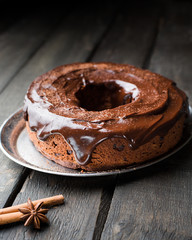 Chocolate cake with nuts, cranberries, chocolate ganache and cocoa powder on dark wooden background with fir tree and spices. Christmas decor of the table. Winter xmas holidays concept. Festive mood