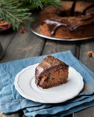 Piece chocolate cake with nuts, cranberries, chocolate ganache and cocoa powder on dark wooden background with fir tree and spices. Christmas decor of the table. Winter xmas holidays concept. 