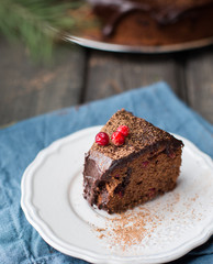 Piece chocolate cake with nuts, cranberries, chocolate ganache and cocoa powder on dark wooden background with fir tree and spices. Christmas decor of the table. Winter xmas holidays concept. 
