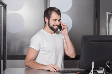 handsome young manager sitting at workplace and talking by phone