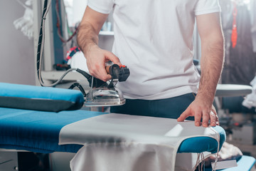 cropped shot of dry cleaning worker using industrial iron at warehouse