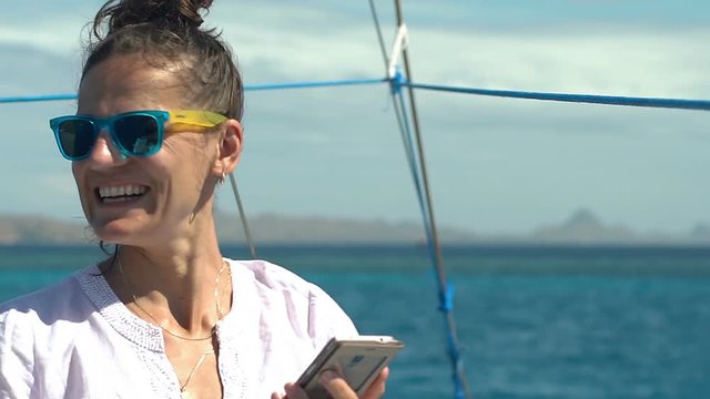 Attractive woman doing selfies on smartphone while relaxing on the boat, steadycam shot
