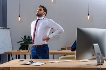 tired businessman standing and stretching in office