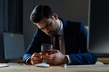 tired drunk businessman looking at glass of whiskey in office