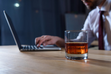 cropped image of businessman working at laptop with glass of whiskey on foreground