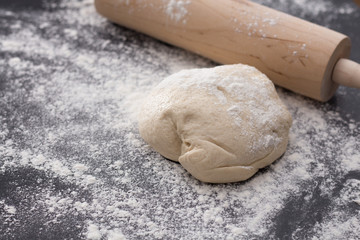 Wooden pin and dough on floured dark surface, baking preparation closeup.