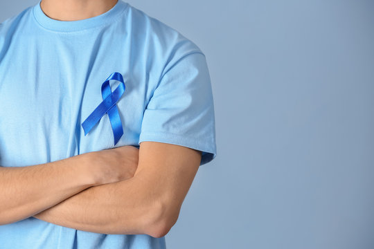 Young man wearing t-shirt with blue ribbon on color background, closeup. Prostate cancer awareness concept