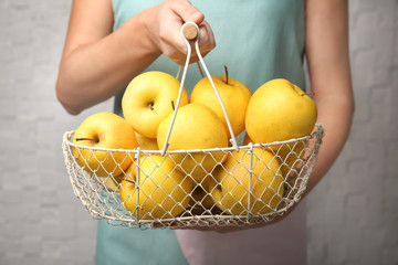 Woman holding metal basket with ripe yellow apples on light background