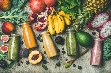 Flat-lay of colorful smoothies in bottles with fresh tropical fruit and superfoods on concrete background, top view. Healthy, clean eating, vegan, vegetarian, detox, dieting breakfast food concept