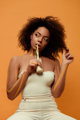 Young sensual african american woman with artistic make-up drinking milk from bottle isolated on orange background
