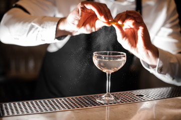 Barman hands sprinkling juice of orange peel into a glass