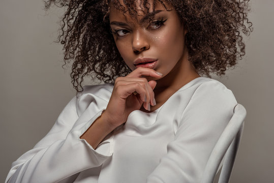 Young sensual african american woman in white shirt with finger on lips isolated on grey background