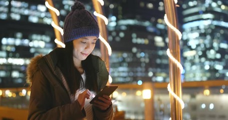 Woman use of smart phone in the city at night, surf online on smart phone with urban city background, woman wearing winter jacket