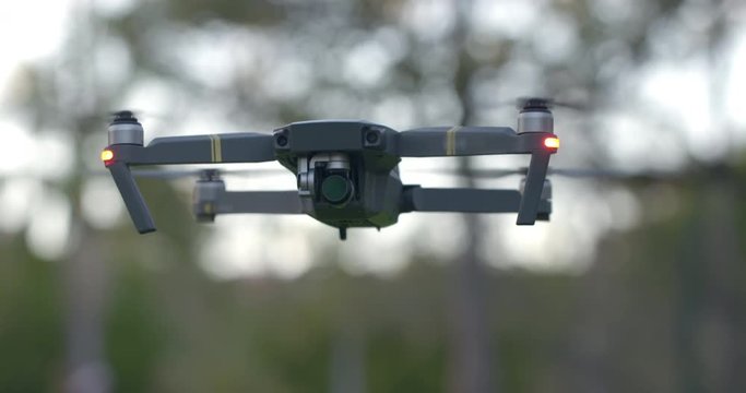 Close view of remote controlled drone with camera flying in a park setting in late afternoon. Slow motion, hand-held 4K.