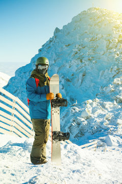 Male snowboarder holding board in hands at the very top of a mountain - outdoors shot