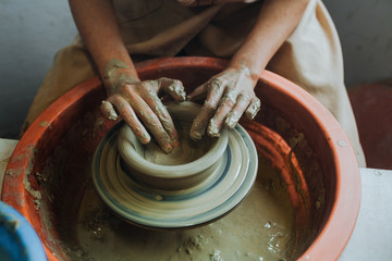 Woman hands makes clay pot on the pottery wheel