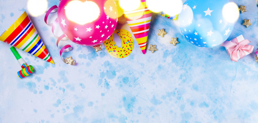 Naklejka premium Bright colorful carnival or party border of balloons, streamers and confetti on blue table. Flat lay style, birthday or party greeting card with copy space and bokeh lights