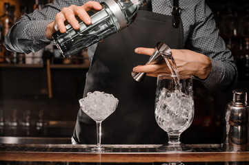 Barmans hands pouring alcoholic drink into a glass using a jigger to prepare a cocktail