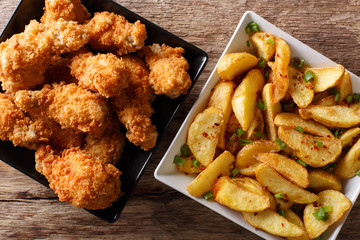 Roasted chicken wings and potato wedges close up. horizontal top view