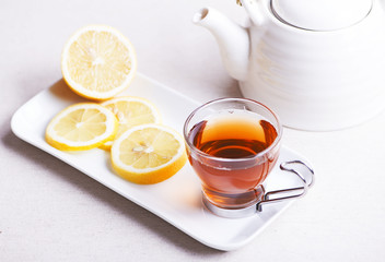 Tea cup with lemon on white plate next to teapot. Infusion.