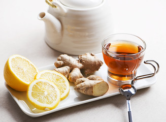 Tea cup with lemon and ginger on white plate next to teapot. Infusion.