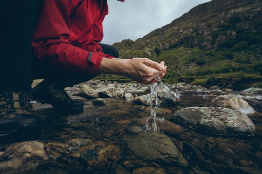 Low section of male hiker drinking water from the stream