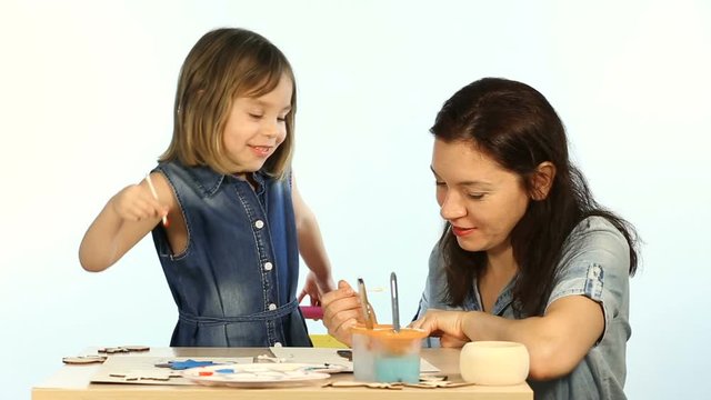 Mom and baby girl paint. Shooting in the studio on a white background. A woman and a child of European appearance.