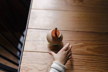 A spinning top on a wooden table. A toddler is reaching for the toy.