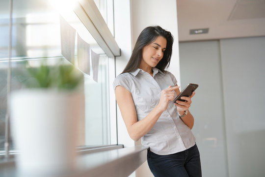 Businesswoman in office relaxing, using smartphone
