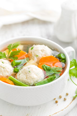 Fresh chicken soup with vegetables and meatballs in a bowl on white background. Top view