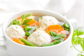 Fresh chicken soup with vegetables and meatballs in a bowl on white background. Top view