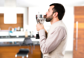 Handsome man with vest holding a trophy inside house